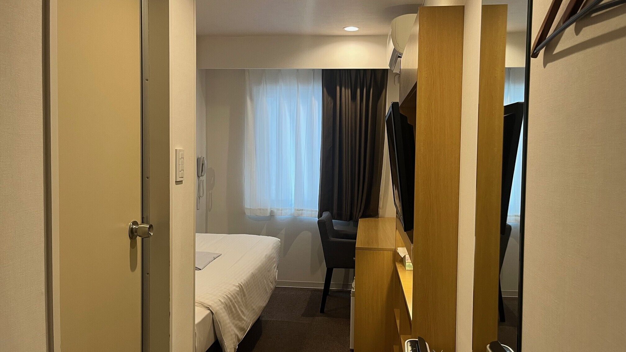 A hotel room with a bed, a desk, a chair, a telephone, and a mirror.