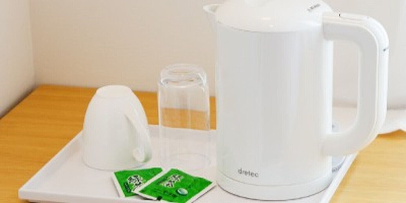 A white electric kettle, a glass pitcher, and two green packets on a white tray.