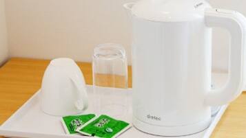 A white electric kettle, a glass pitcher, and two green packets on a white tray.