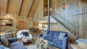 A spacious living area with a high ceiling, wooden walls, a staircase, and a dining area. - Chic Lake Arrowhead Retreat: 4 Seasons of Fun! (Lake Arrowhead)