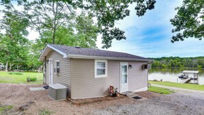 A small, single-story cabin with a gravel driveway, a front door, and a small porch area. - Lake of the Ozarks Cabin w/ Private Dock + Kayaks (Lincoln)