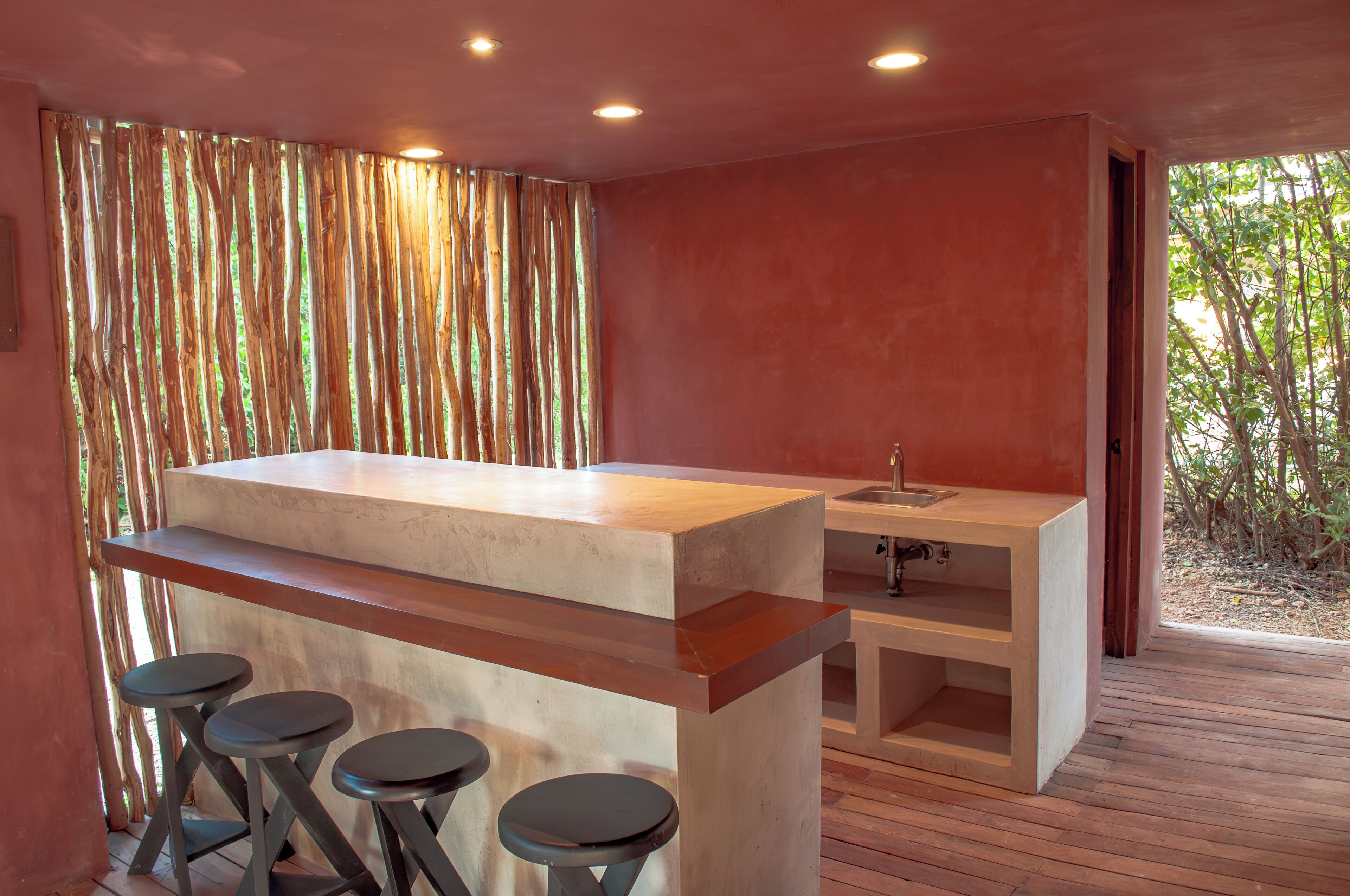 A modern kitchen with a central island, bar stools, and a view of greenery outside.