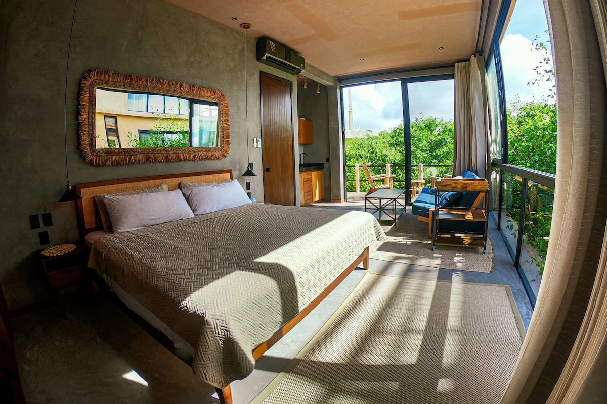 A bedroom with a large bed, a mirror, and a balcony with seating.