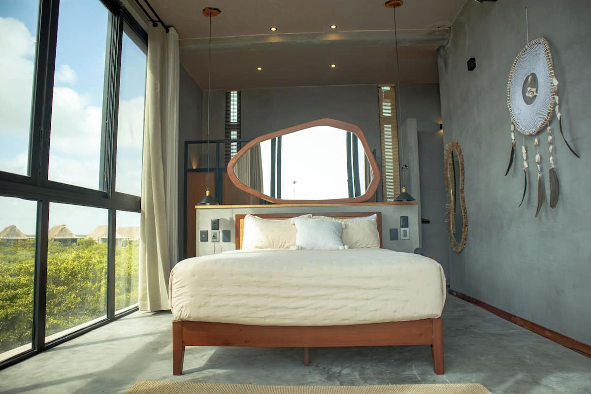 A bedroom with a large bed, a mirror, and a view of the outdoors.