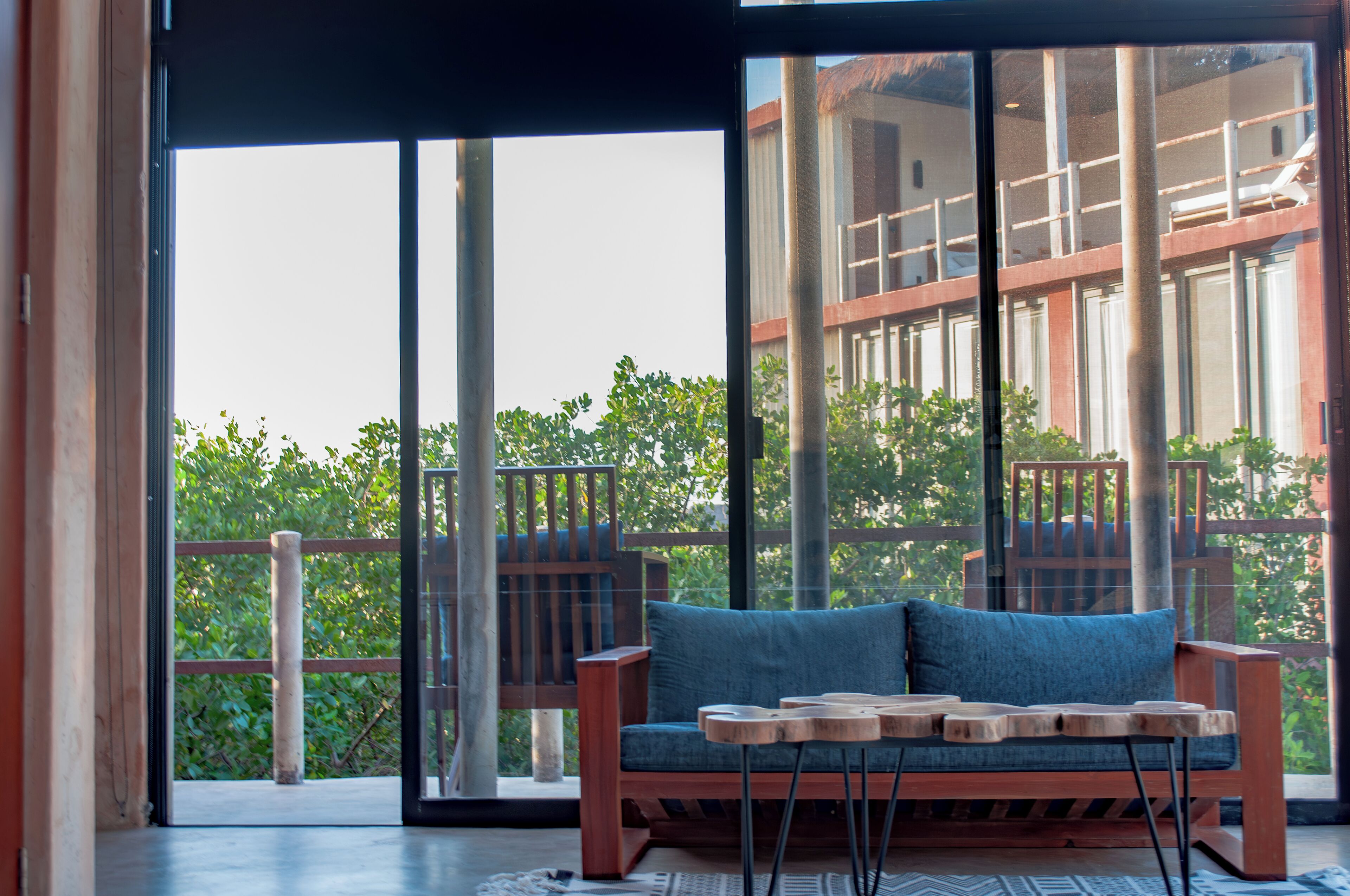 A balcony with a wooden bench and a small table, large glass doors, and a view of greenery.