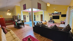Un vaste espace de vie comprenant un canapé, une table à manger et des chaises, un escalier menant à un niveau supérieur, et un téléviseur fixé au mur.
