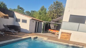 A swimming pool with a wooden deck, lounge chairs, and a covered seating area. - 2-room luxury apartment  (Juvignac)