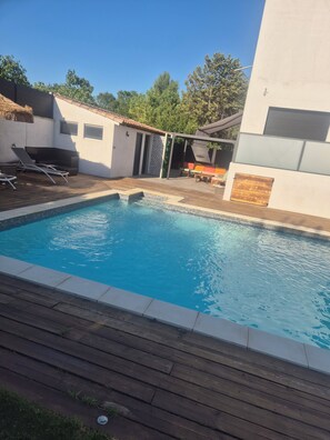 A swimming pool with a wooden deck, lounge chairs, and a covered seating area. - 2-room luxury apartment  (Juvignac)