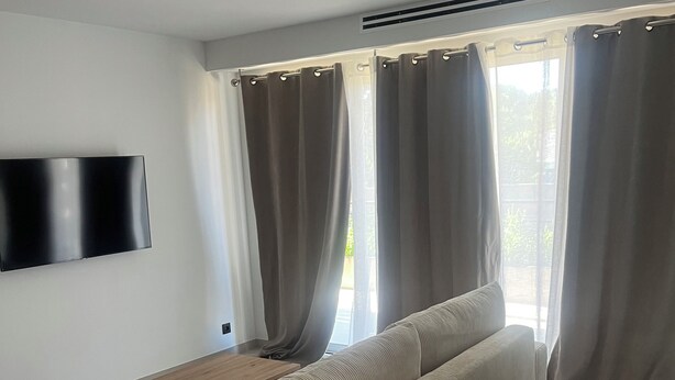 A modern living room with a sofa, a coffee table, and a flat-screen TV mounted on the wall. - 2-room luxury apartment  (Juvignac)