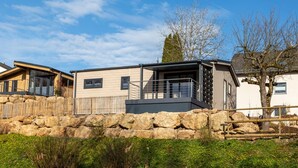 Un bâtiment moderne doté d’un mur de soutènement en pierre, d’un balcon et d’un arbre en arrière-plan.