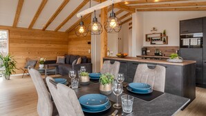 A modern kitchen with wooden beams, a dining area with blue plates, and a cozy seating area with a sofa and cushions. - Chalet Seeblick I Terrace I View I Hiking (Hillesheim)