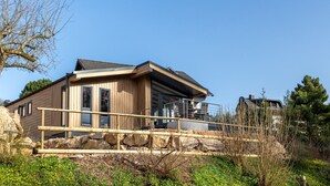 A modern wooden house with a balcony, situated on a rocky terrain with sparse vegetation. - Chalet Seeblick I Terrace I View I Hiking (Hillesheim)
