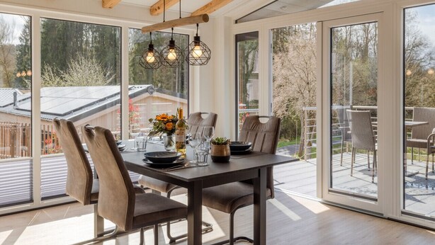 A dining area with a table set for four, large windows, and a view of the outdoors. - Chalet Seeblick I Terrace I View I Hiking (Hillesheim)