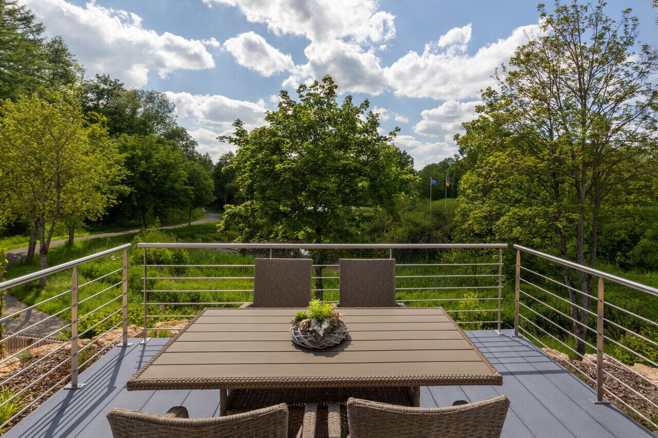 A deck with a table and chairs, surrounded by a metal railing, overlooking a lush green landscape.