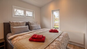 Een slaapkamer met een bed, twee ramen, een radiator en een klein plantje.