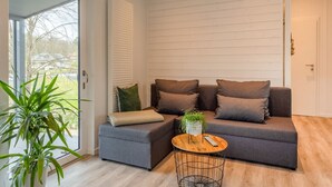 Een moderne woonkamer met een grijze bank, een klein rond houten bijzettafeltje en een potplant.