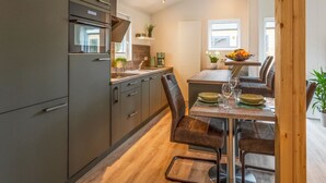 Een moderne keuken met inbouwapparatuur, een eethoek met een houten tafel en stoelen, en uitzicht op buiten door een raam.