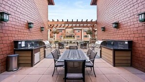 Eine Außenpatio mit Grill, Esstisch und Stühlen, umgeben von Ziegelmauern und einer Pergola.