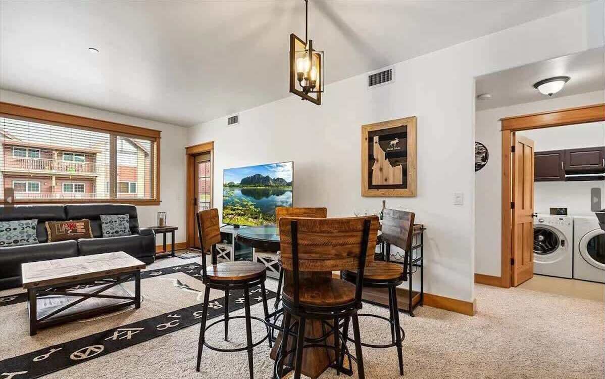 Ein Wohnzimmer mit einer Couch, einem Couchtisch und Stühlen, ein Essbereich mit Tisch und Stühlen, ein Gemälde und eine Waschküche mit Waschmaschine.