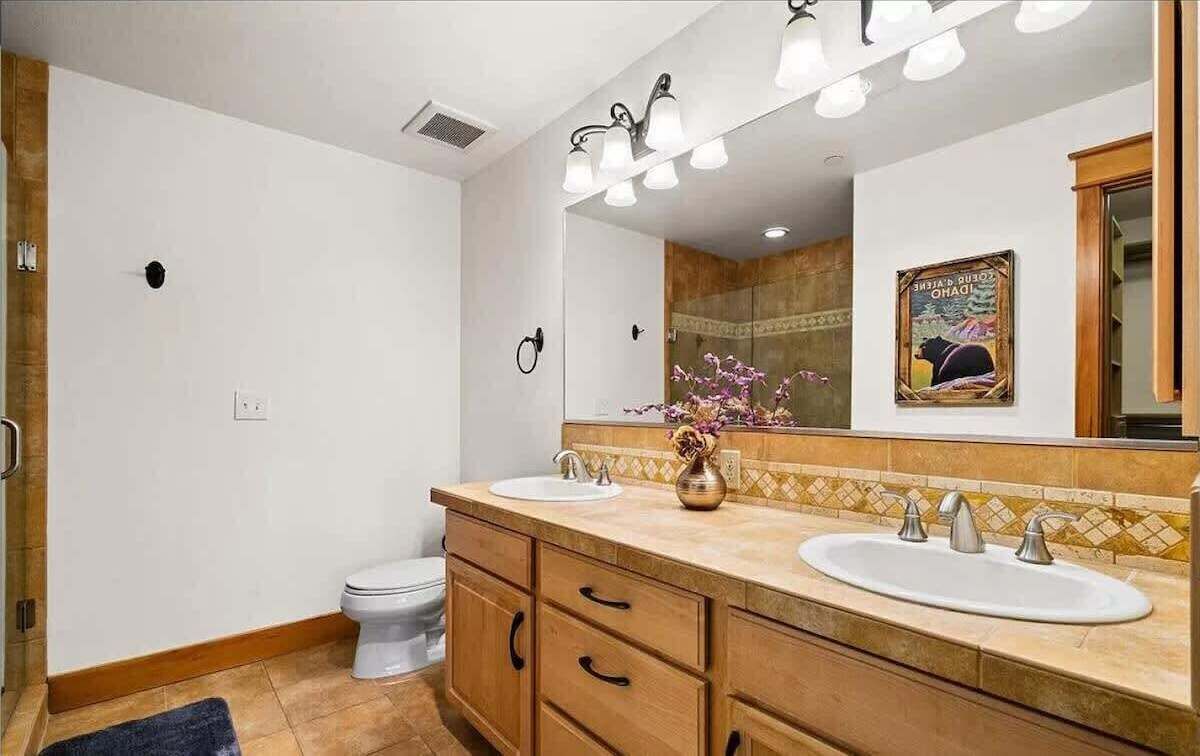 Un baño con dos lavamanos, un inodoro, una ducha y un espejo grande.