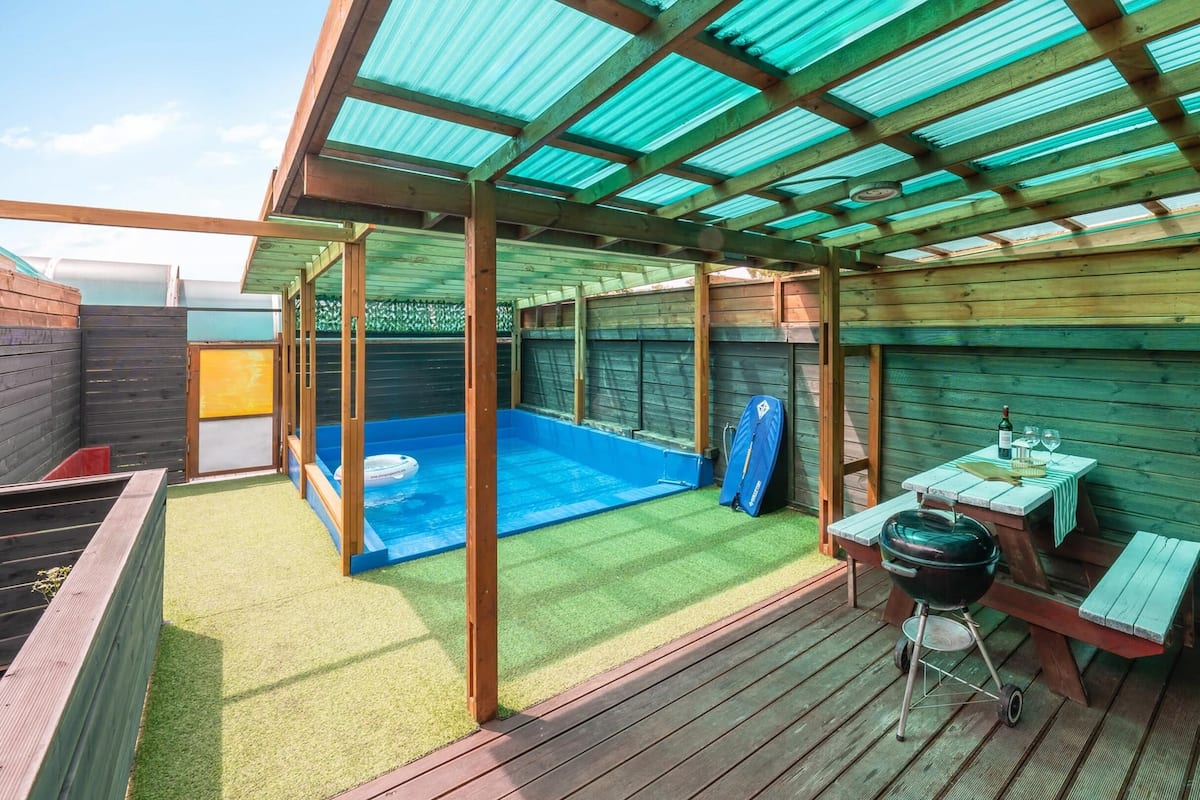 A covered outdoor area with a pool, a barbecue setup, and a table with a bottle and glass.