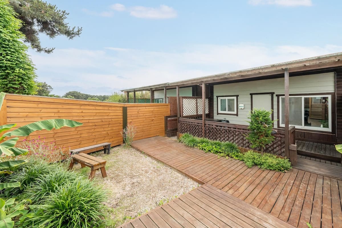 A wooden deck with a wooden fence, a bench, and a small garden area with plants and a tree.