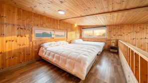 A wooden-paneled room with a large bed, two windows, and a view of the outdoors.