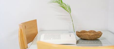Un serre-livre en bois, un livre et un panier tressé sont posés sur une table, à côté d’un vase en verre transparent contenant une seule plante verte.