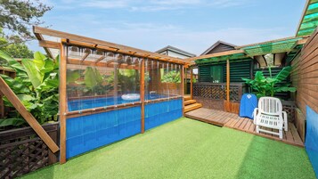 Un patio trasero con piscina, césped artificial y una terraza de madera.