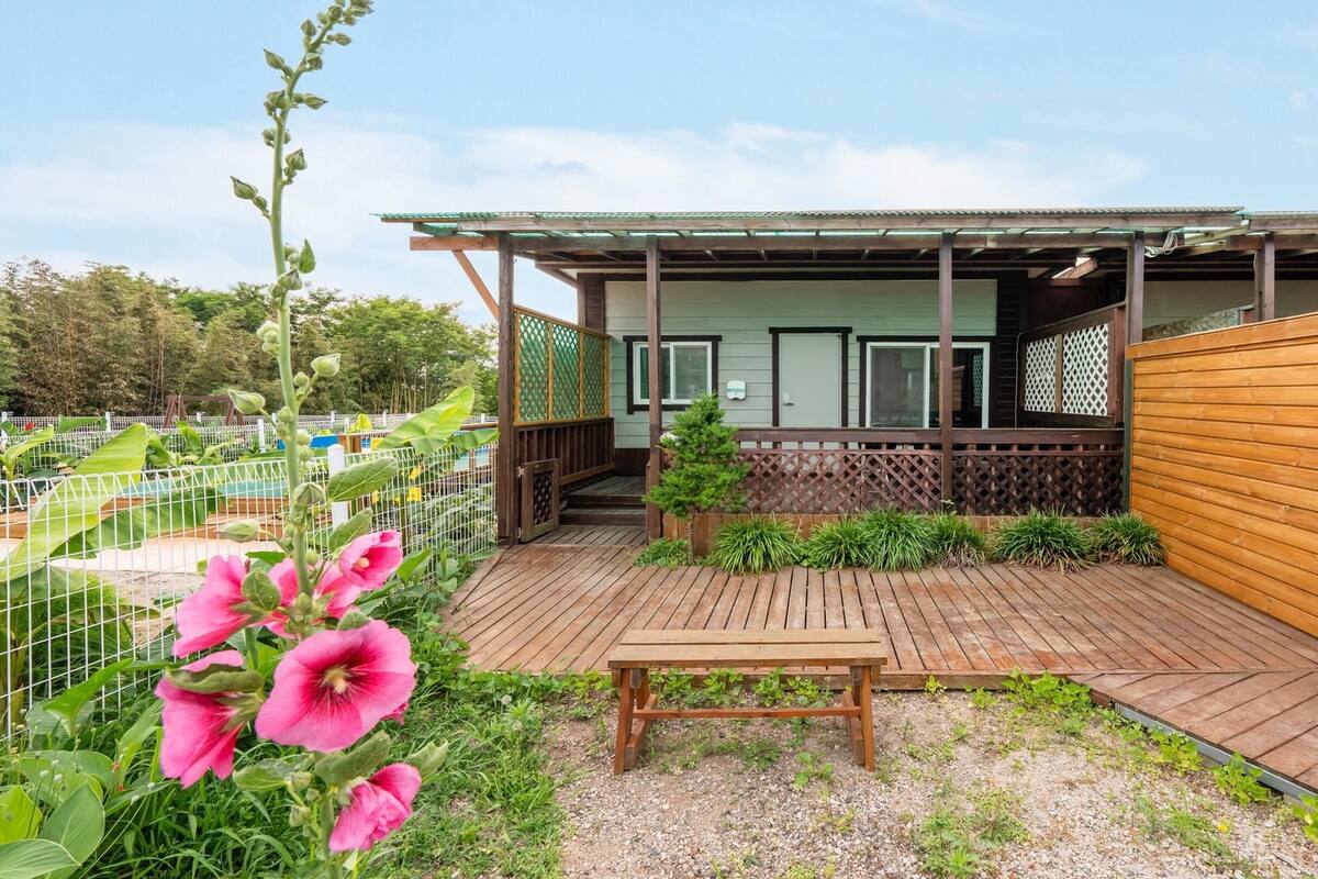 A wooden deck with a bench, a small garden area with plants, and a building with a covered porch.