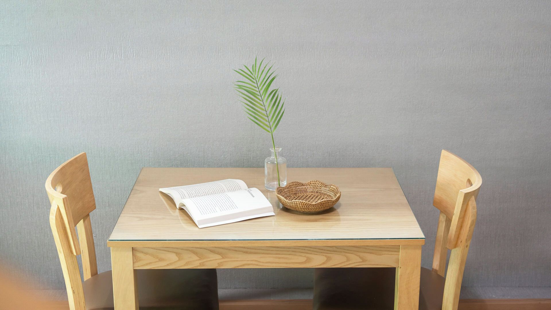 A wooden table with a book, a glass vase with a plant, and a woven basket.