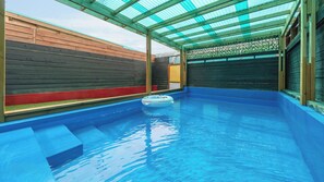 Una piscina interior con techo de vidrio, paredes de madera y un flotador.