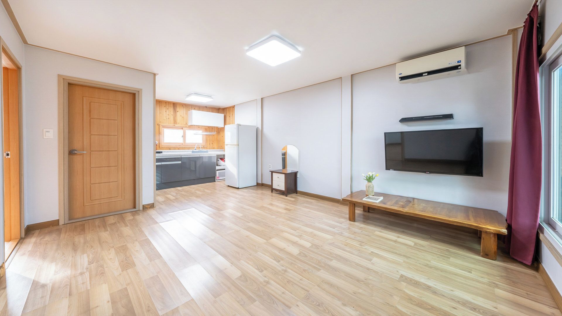 Un vaste espace de vie doté d’un plancher en bois, d’un téléviseur à écran plat fixé au mur et d’un petit banc.