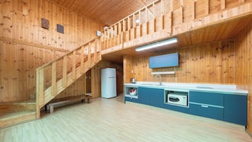 A wooden interior with a kitchen area, including a microwave, sink, and a refrigerator.