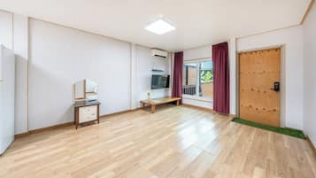 Una habitación con piso de madera, puerta de madera, un banco, una mesita con un espejo y un televisor en la pared.