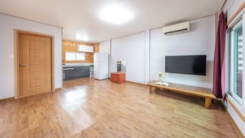 A spacious living area with a wooden floor, a flat-screen TV mounted on the wall, a bench, and a small table with a plant.