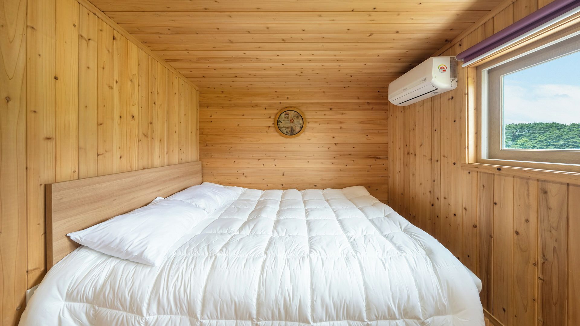 A single bed with white bedding in a wooden room with a window and an air conditioning unit.