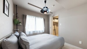 Une chambre à coucher comprenant un lit, un ventilateur de plafond, une fenêtre avec des rideaux et une porte donnant sur un placard.