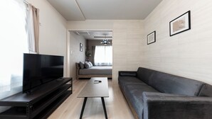 Un salon moderne avec un téléviseur à écran plat posé sur un meuble noir, un canapé gris, une table basse et un mur de couleur claire orné de tableaux.