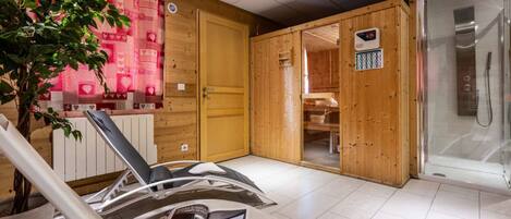 A sauna room with wooden walls, a glass door leading to a shower area, and a magazine on a chair.
