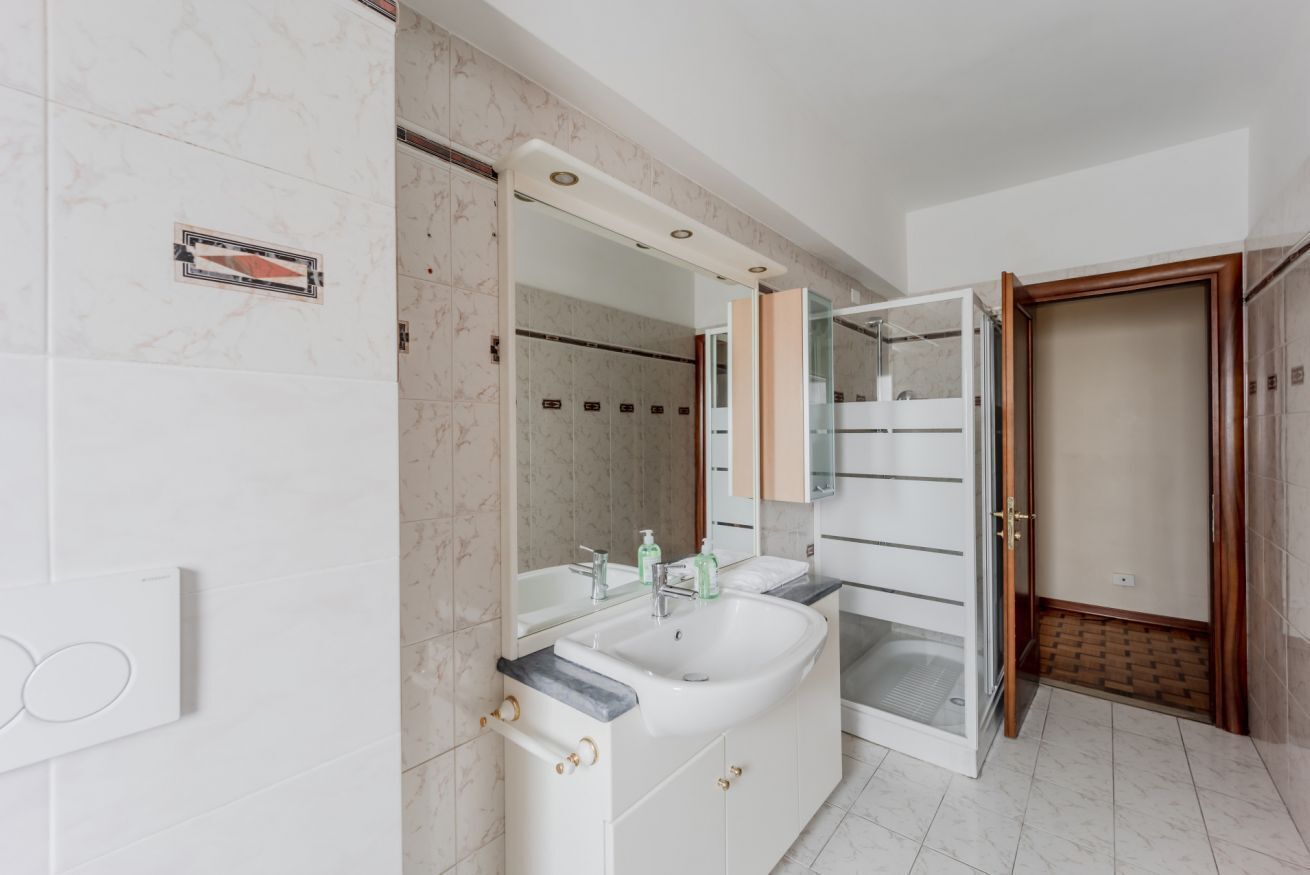 A bathroom with a large mirror, a sink, and a shower enclosure.