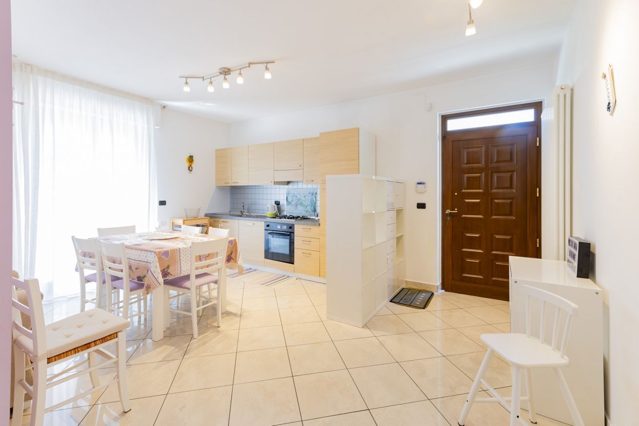 A modern kitchen with white cabinets, a dining area with white chairs, and a wooden door.