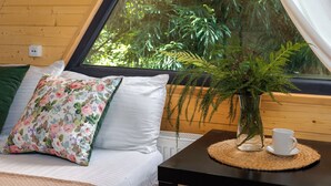 Una habitación acogedora con una cama, una mesa con una taza y un florero, y una ventana con vistas al verdor.