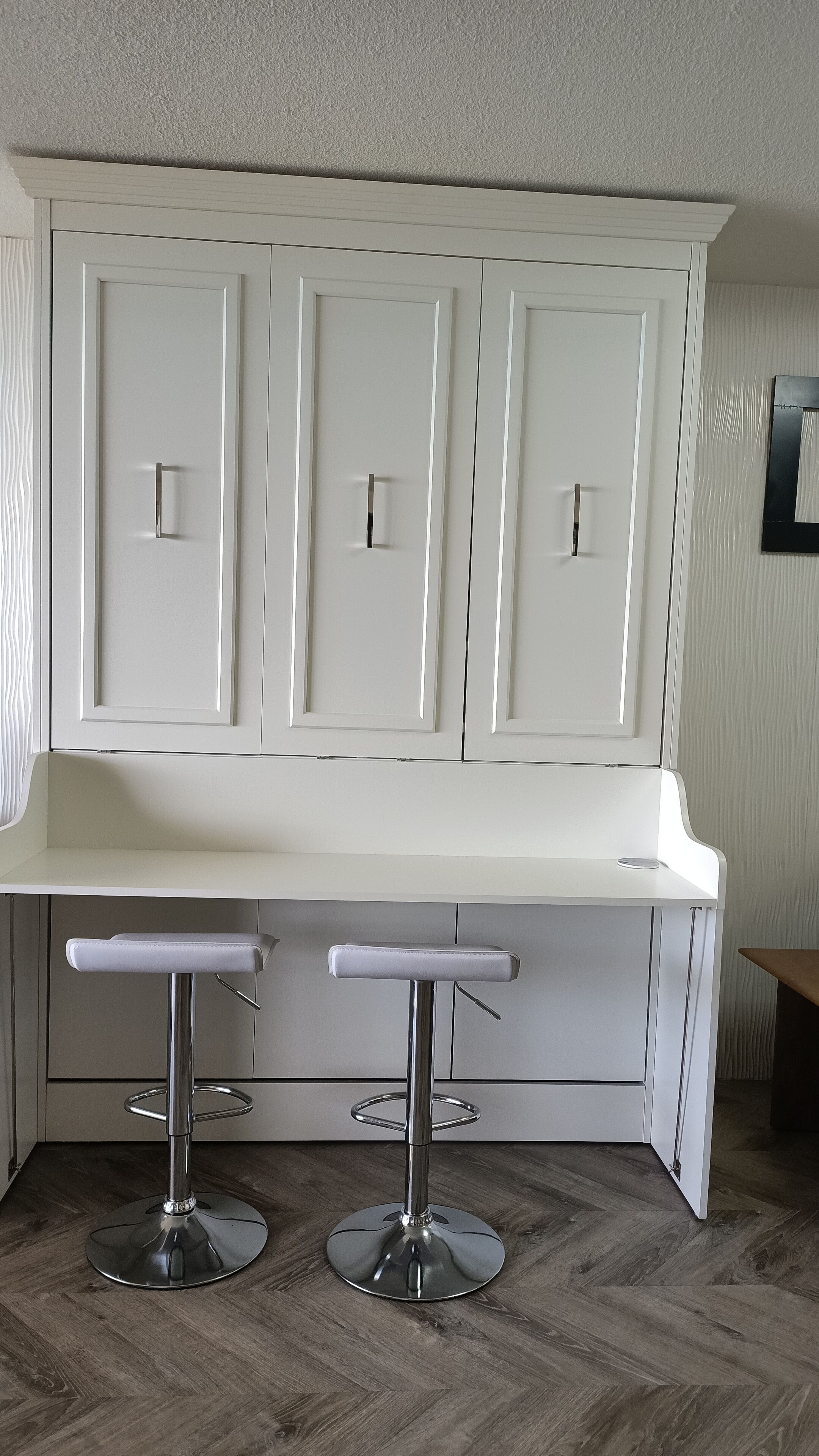 A kitchen with white cabinets, a white countertop, and two bar stools with metal bases.