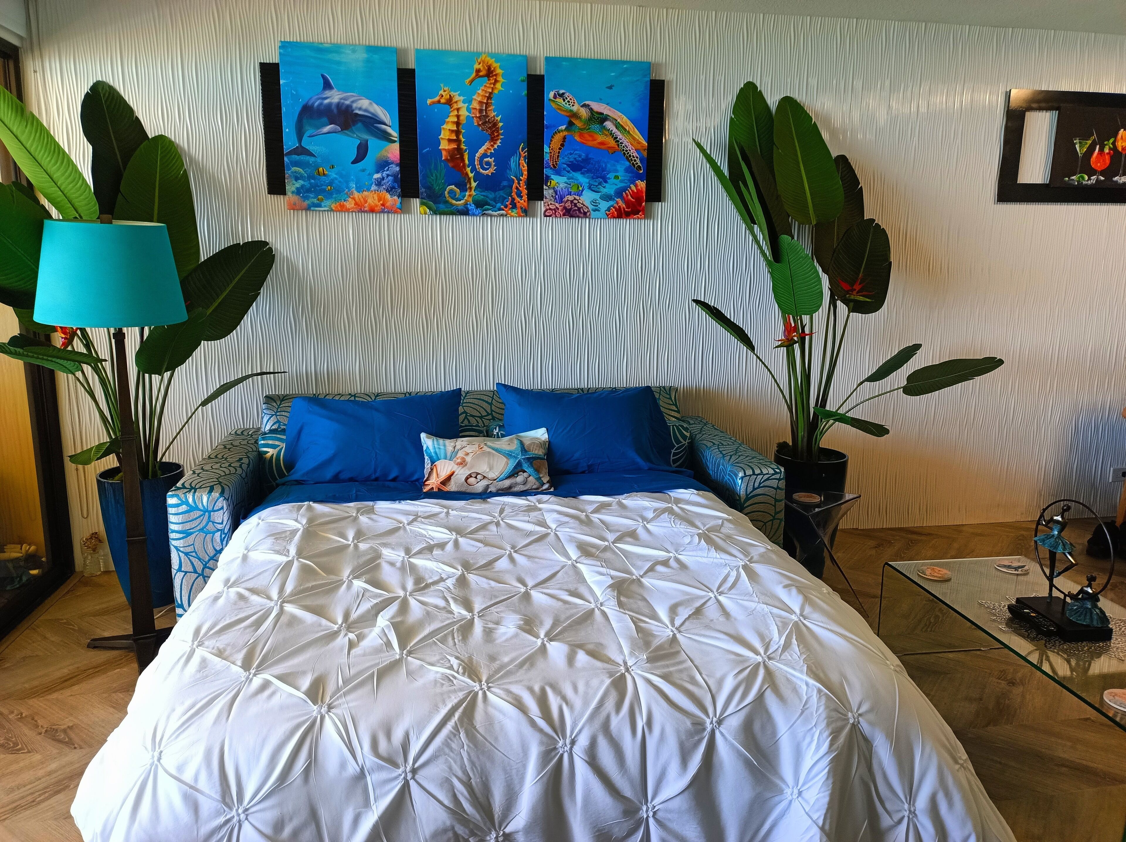 Ein Schlafzimmer mit einem Bett, Bettwäsche in Blau und Weiß sowie drei Bildern an der Wand, die Meereslebewesen zeigen.