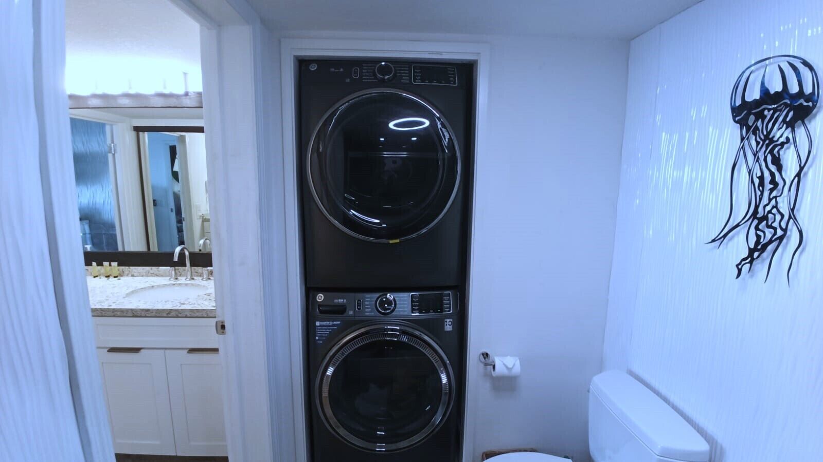 Une petite buanderie équipée de deux machines à laver superposées et de toilettes.