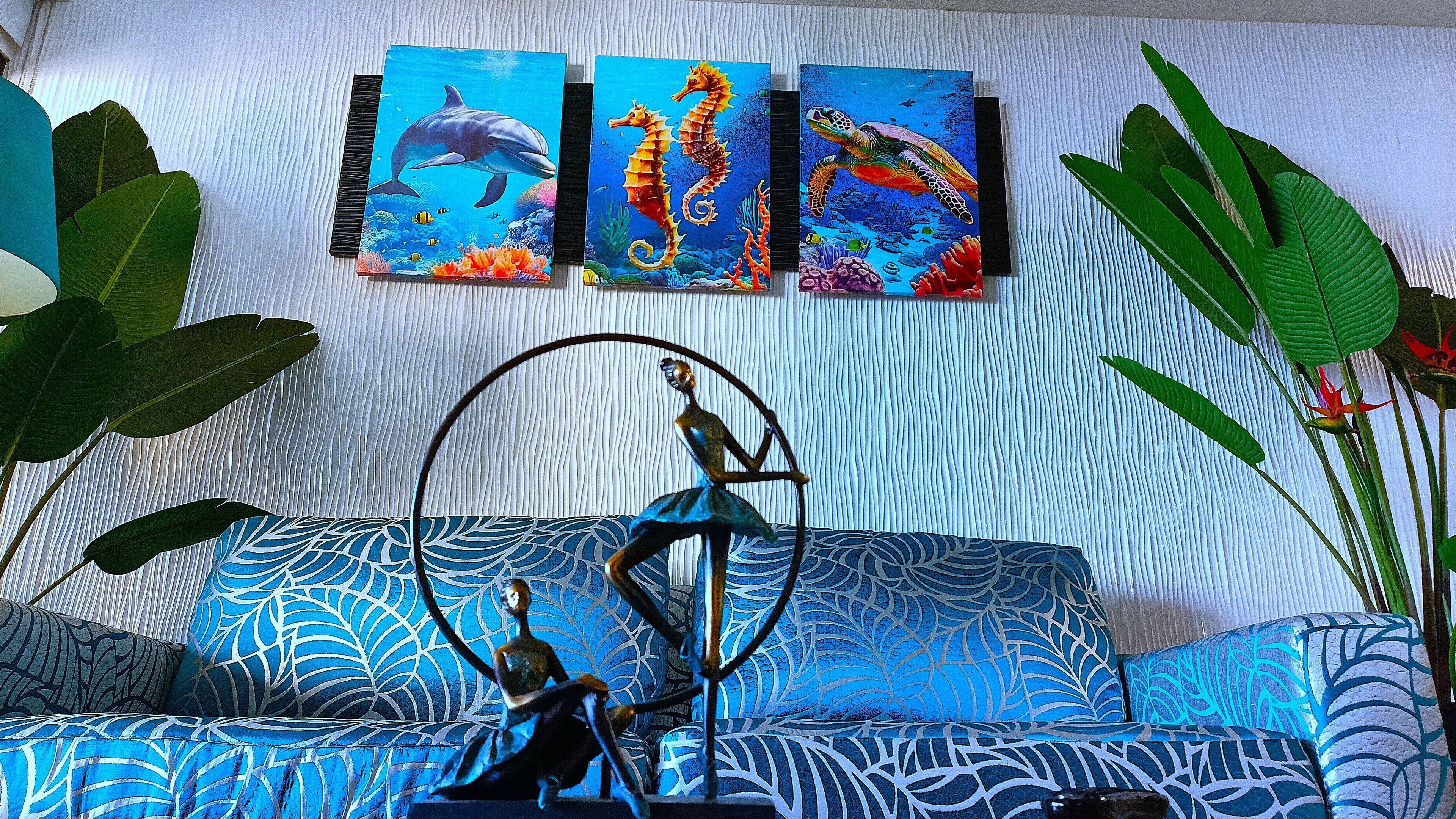 Ett rum med en mönstrad soffa, en skulptur och tre tavlor med motiv av marint liv på väggen.