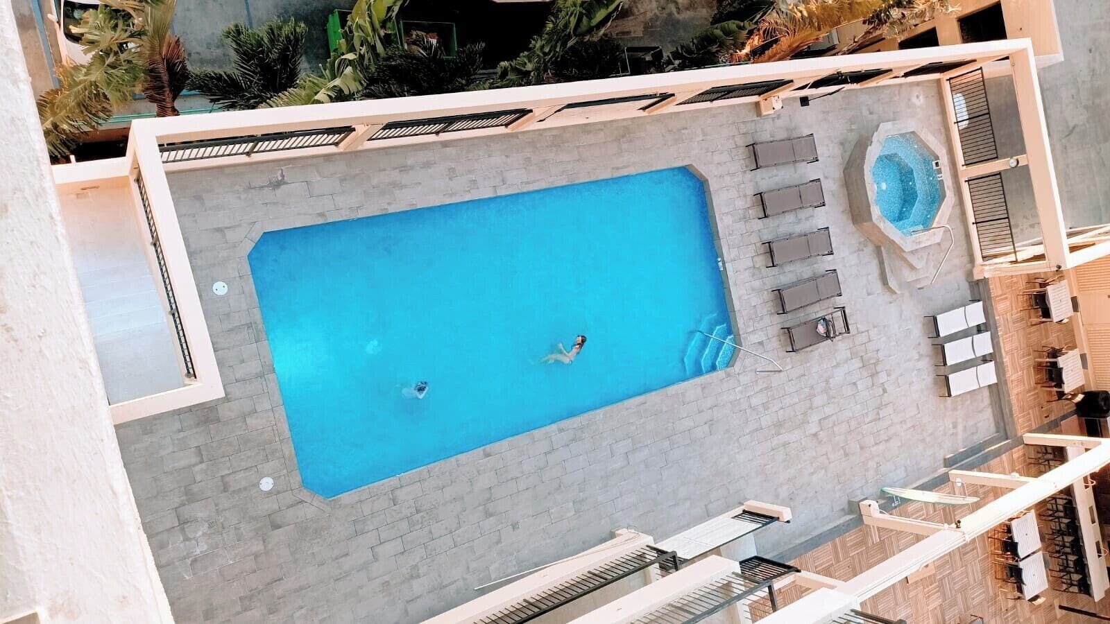 An aerial view of a swimming pool with two people, a hot tub, and outdoor seating.