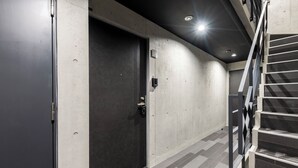 En hall med en mörk dörr, en trappa och en lampa i taket.