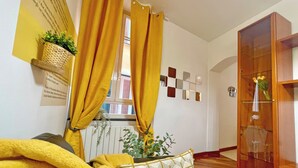 A room with a wooden floor, a window with yellow curtains, a wall-mounted mirror, and a wooden cabinet. - Happy Family Apartments Andreana (Genoa)